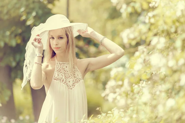 ドレスと帽子を身に着けているブロンドの女性が咲く庭でポーズ — ストック写真