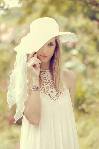 ブロンド女性で帽子Posing上のぼやけた庭の背景 — ストック写真