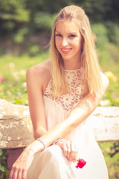 Smiling blonde woman posing sitting on bench in summer garden