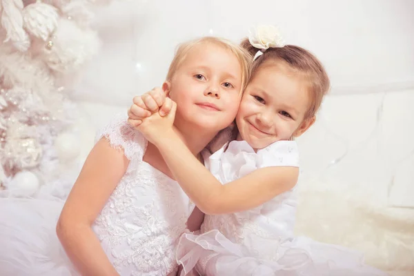 Δύο μικρά κορίτσια στα λευκά φορέματα κοντά σε ένα χριστουγεννιάτικο δέντρο με τα νέα — Φωτογραφία Αρχείου