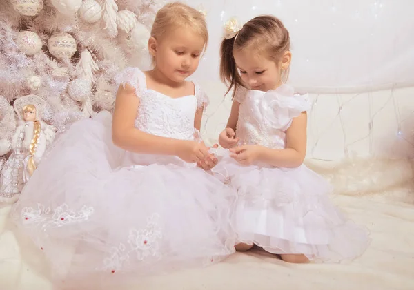 Dos niñas en vestidos blancos cerca de un árbol de Navidad con nuevo —  Fotos de Stock