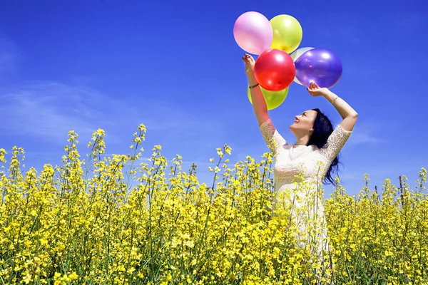 Donna che tiene palloncini colorati nel campo di senape in una giornata di sole — Foto Stock