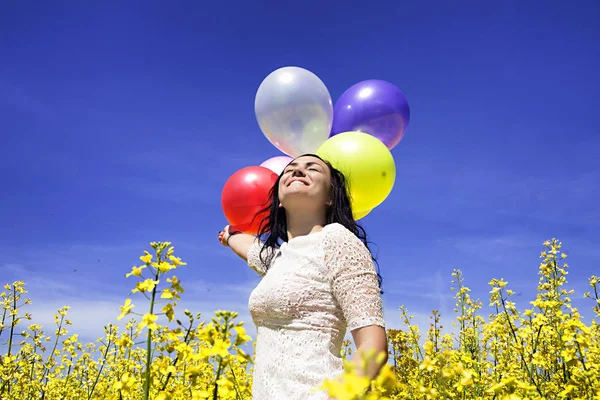 Woman holding colorful balloons in mustard field on a sunny day — Stock Photo, Image