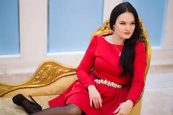 Giovane donna in abito rosso su divano dorato — Foto Stock
