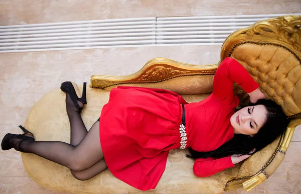 Όμορφη σέξι νεαρή γυναίκα με κόκκινο φόρεμα σε Χρυσή καναπέ — Φωτογραφία Αρχείου