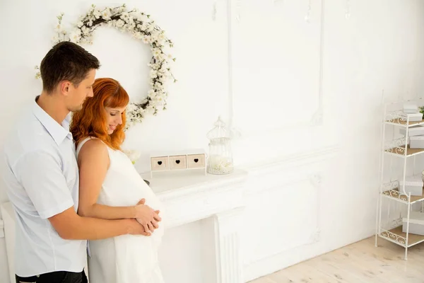 A pregnant wife and husband stand in white decoration — Stock Photo, Image