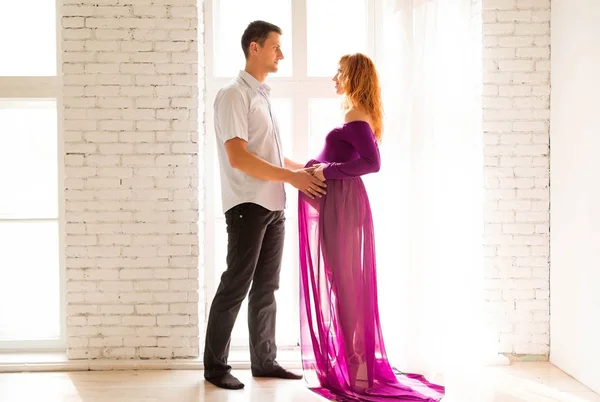 Молодой человек обнимает красивую беременную девушку в фиолетовом платье — стоковое фото