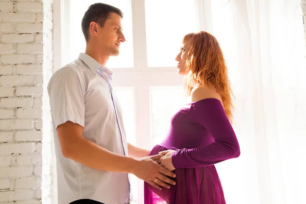 Een jonge man is een mooi zwanger meisje knuffelen in een paarse jurk — Stockfoto