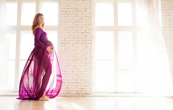 Mulher grávida em vestido roxo na sala branca — Fotografia de Stock