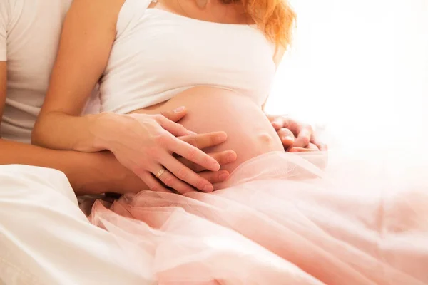 Две пары рук на голом животе беременной женщины — стоковое фото