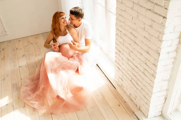 Schwangere im Tüllrock und ihr Mann sitzen auf dem Boden neben einem großen Fenster — Stockfoto