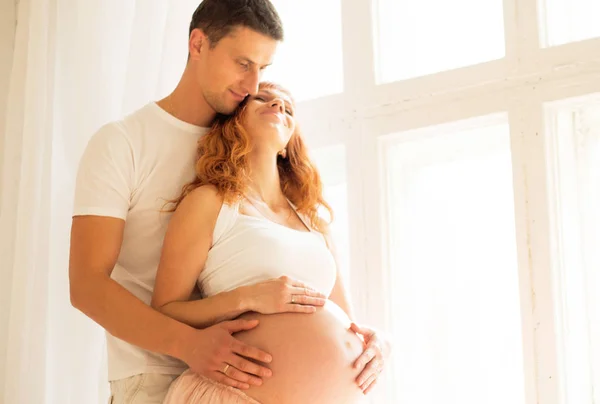 Zwangere vrouw in een Tule rok en haar man zijn in de buurt van een groot raam — Stockfoto