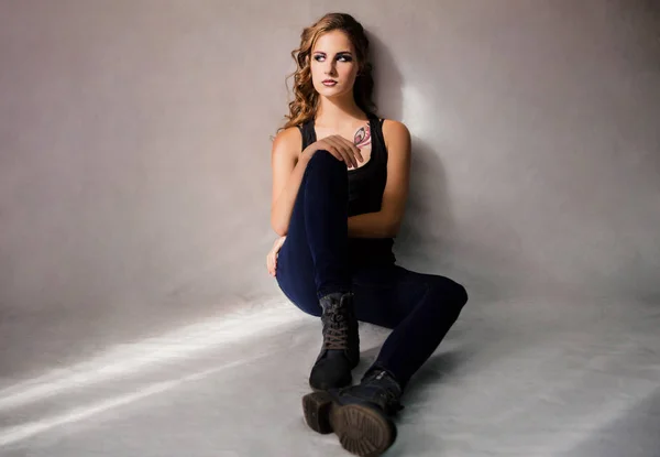 Krásná dívka model sedí v džínách a tričku na podlaze — Stock fotografie