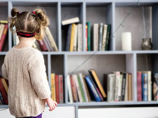 Una niña elige un libro en su biblioteca — Foto de Stock