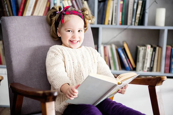 Niña con un libro en sus manos se sienta en una silla — Foto de Stock