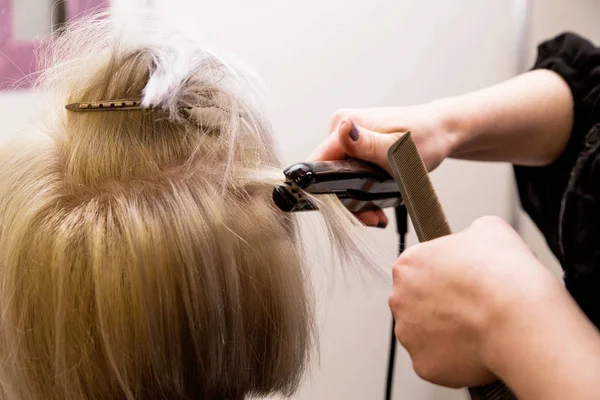 The hairdresser straightens  hair with an iron — Stock Photo, Image