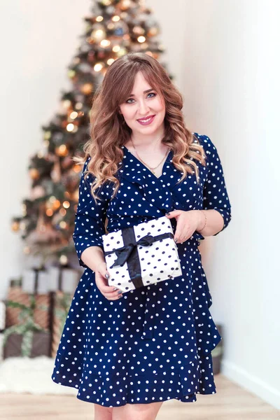 Hermosa chica en un vestido azul con un regalo en sus manos. Árbol de Navidad en el fondo — Foto de Stock