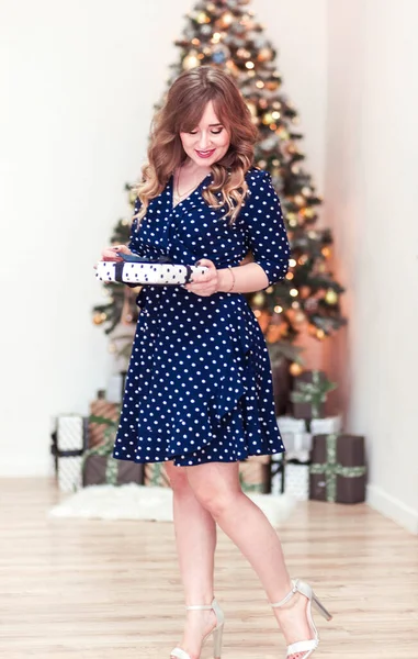 Красивая девушка в синем платье с подарком в руках. Рождественская елка на заднем плане — стоковое фото