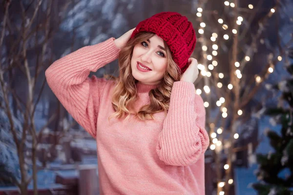 Piękna dziewczyna w różowym swetrze i czerwonym kapeluszu patrzy w kamerę i uśmiecha się — Zdjęcie stockowe