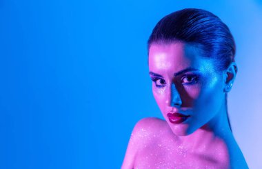 Stüdyoda renk filtreli güzel bir esmer model var. Moda, güzellik, ışıltı. Neon ışıklı, mor ve mavi elbiseli güzel esmer bir kadının yakın çekimi..