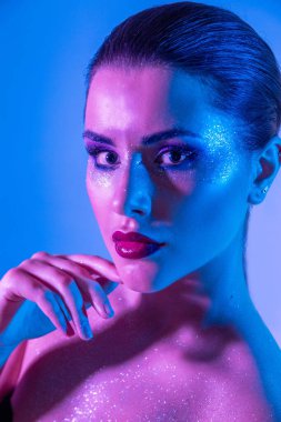 Stüdyoda renk filtreli güzel bir esmer model var. Moda, güzellik, ışıltı. Neon ışıklı, mor ve mavi elbiseli güzel esmer bir kadının yakın çekimi..