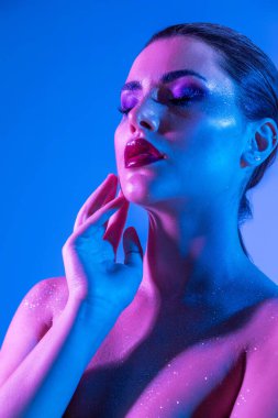 Stüdyoda renk filtreli güzel bir esmer model var. Moda, güzellik, ışıltı. Neon ışıklı, mor ve mavi elbiseli güzel esmer bir kadının yakın çekimi..