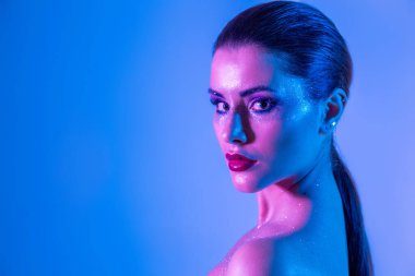 Stüdyoda renk filtreli güzel bir esmer model var. Moda, güzellik, ışıltı. Neon ışıklı, mor ve mavi elbiseli güzel esmer bir kadının yakın çekimi..