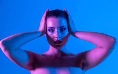 Stüdyoda renk filtreli güzel bir esmer model var. Manken kafasını eline aldı. Neon ışıklı, mor ve mavi elbiseli güzel esmer bir kadının yakın çekimi.