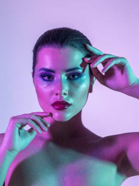 Stüdyoda renk filtreli güzel bir esmer model var. Moda, güzellik, ışıltı. Neon ışıklı, mor, mavi ve yeşil renkli güzel esmer bir kadının yakın çekim tarafı.