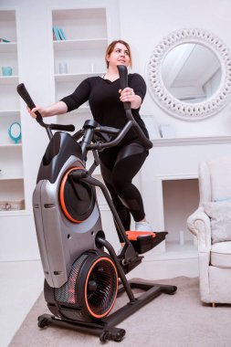 Manken - şişman bir kadın, kilo vermeye çalışıyor ve evde eliptik bir eğitmenle meşgul.