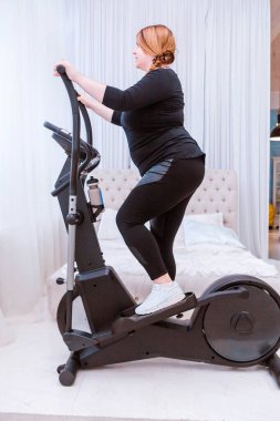 Manken - şişman bir kadın, kilo vermeye çalışıyor ve evde eliptik bir eğitmenle meşgul.