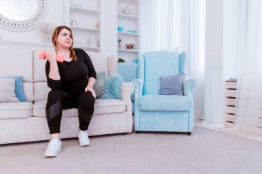 Model - şişman bir kadın, kilo vermeye çalışıyor ve evde halterlerle egzersiz yapıyor..