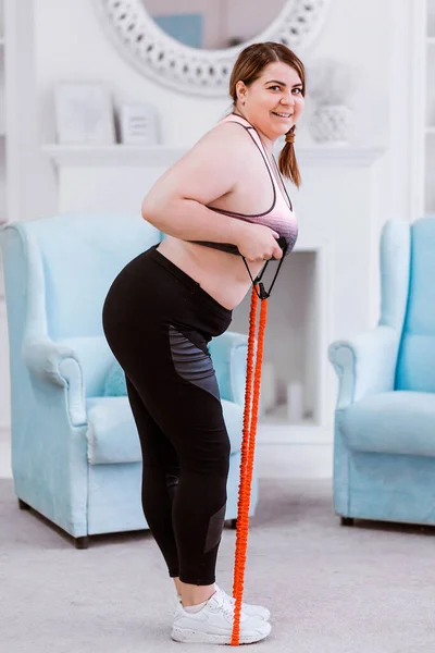 Le modèle est une femme grosse, essayant de perdre du poids à la maison et faire des exercices avec un extenseur — Photo