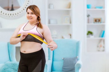 Manken - şişman bir kadın, ölçü bandıyla belin ölçüsünü alıyor.