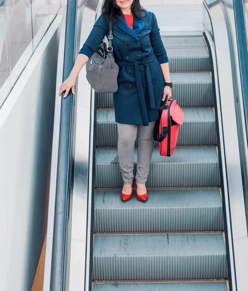 Женщина с красным чемоданом спускается на эскалаторе в бизнес-центре — стоковое фото