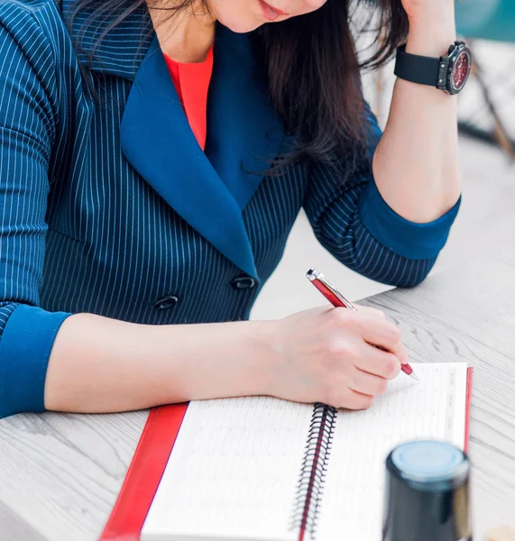 Geschäftsfrau in blauer Jacke schreibt etwas auf Papier. Auf dem Tisch liegt ein Stempel — Stockfoto