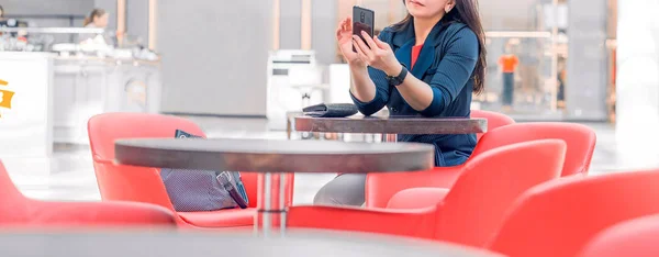 Geschäftsfrau in blauer Jacke sitzt in einem Einkaufszentrum oder Business Center in einem Café mit roten Stühlen und telefoniert — Stockfoto