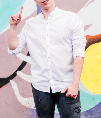 Beyaz gömlekli ve siyah kotlu genç bir adam elini kaldırdı ve işaret parmağıyla yukarı doğru işaret etti.