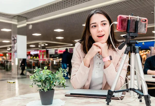 Alışveriş merkezindeki genç bir kadın blogcu dizüstü bilgisayarda çalışıyor, canlı yayınlar yapıyor, videoları kaydediyor, sosyal ağlarının takipçileriyle iletişim kuruyor.