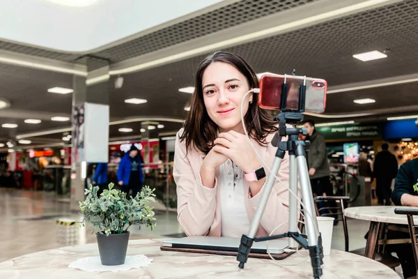 A young woman blogger in a shopping center works at a laptop, conducts live broadcasts, records videos, communicates with followers of her social networks — Stock Photo, Image