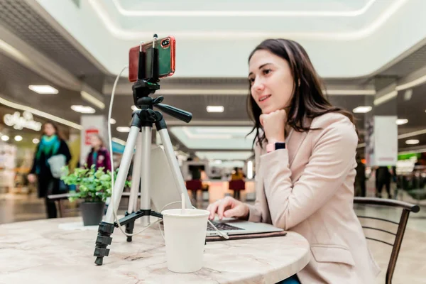 Une jeune blogueuse dans un centre commercial travaille sur un ordinateur portable, diffuse en direct, enregistre des vidéos, communique avec les abonnés de ses réseaux sociaux — Photo