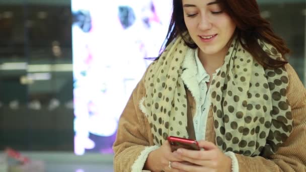 Молода жінка в торговому центрі користується мобільним телефоном. Грабує щось, виглядає і посміхається. — стокове відео