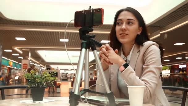 Una joven bloguera en un centro comercial trabaja en una computadora portátil, realiza transmisiones en vivo, graba videos, se comunica con seguidores de sus redes sociales — Vídeo de stock