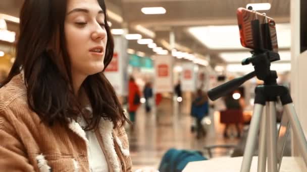 Una joven bloguera en un centro comercial trabaja en una computadora portátil, realiza transmisiones en vivo, graba videos, se comunica con seguidores de sus redes sociales — Vídeo de stock