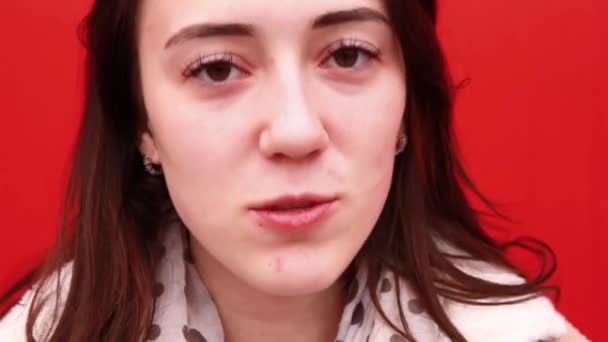 Une jeune blogueuse se tient devant le mur rouge, regarde la caméra et dit quelque chose . — Video