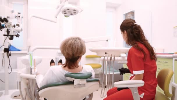 Minsk, Vitryssland - 21 november 2019.Ung kvinnlig tandläkare i röd kostym undersöker en patient — Stockvideo