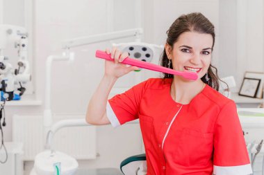 Modern klinikte büyük bir diş fırçasını gösteren kadın dişçi ya da hijyenistin portresi