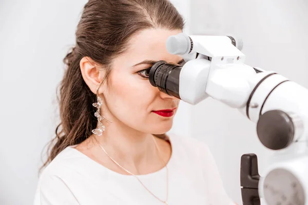 Attractive young female dentist in a white suit uses a microscope at work — Stock Photo, Image