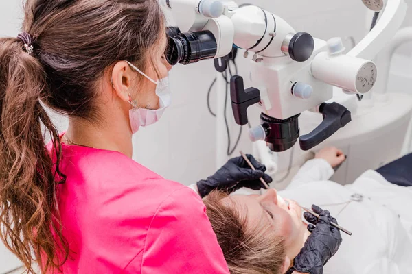 A female professional dentist examines a female patient with a stamotologic microscope in her office. Stamotologist profession concept