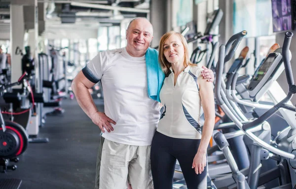 Happy older married couple in the gym. Hugs and looks at the camera